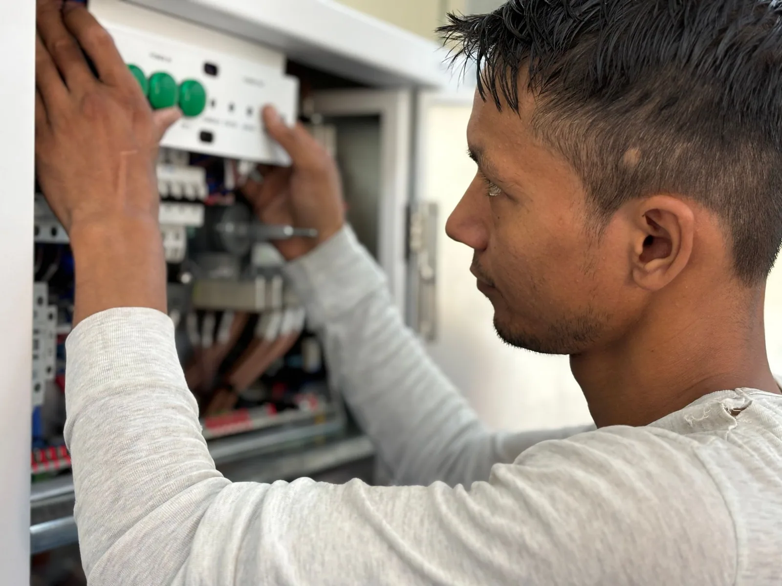 Électricien de dos devant un tableau électrique neuf, en train de repérer les circuits