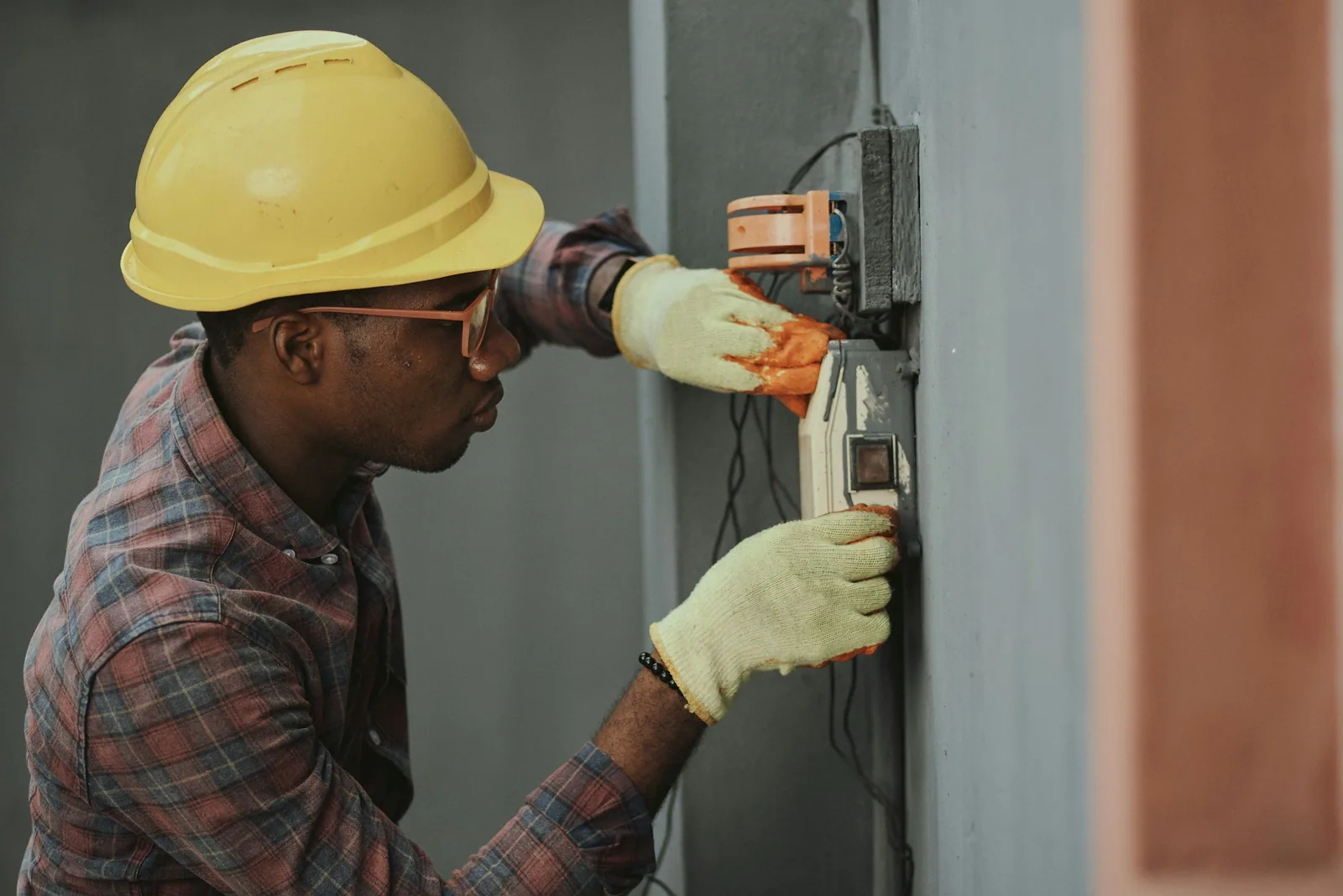 Électricien casqué et ganté qui intervient sur un boîtier électrique fixé au mur