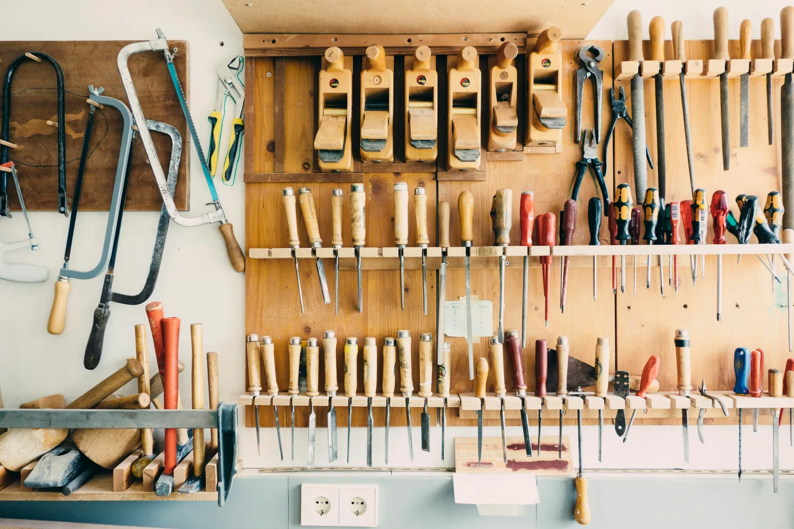 Mur d’outils de l’atelier : scies, rabots, ciseaux et tournevis rangés sur des panneaux de bois