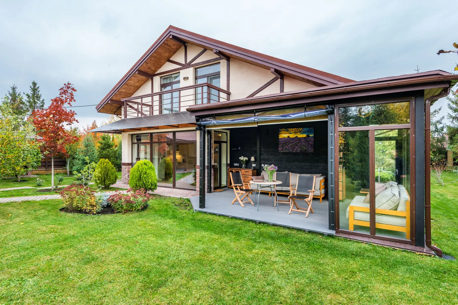 Maison à colombages avec une terrasse couverte vitrée ouverte sur le jardin.