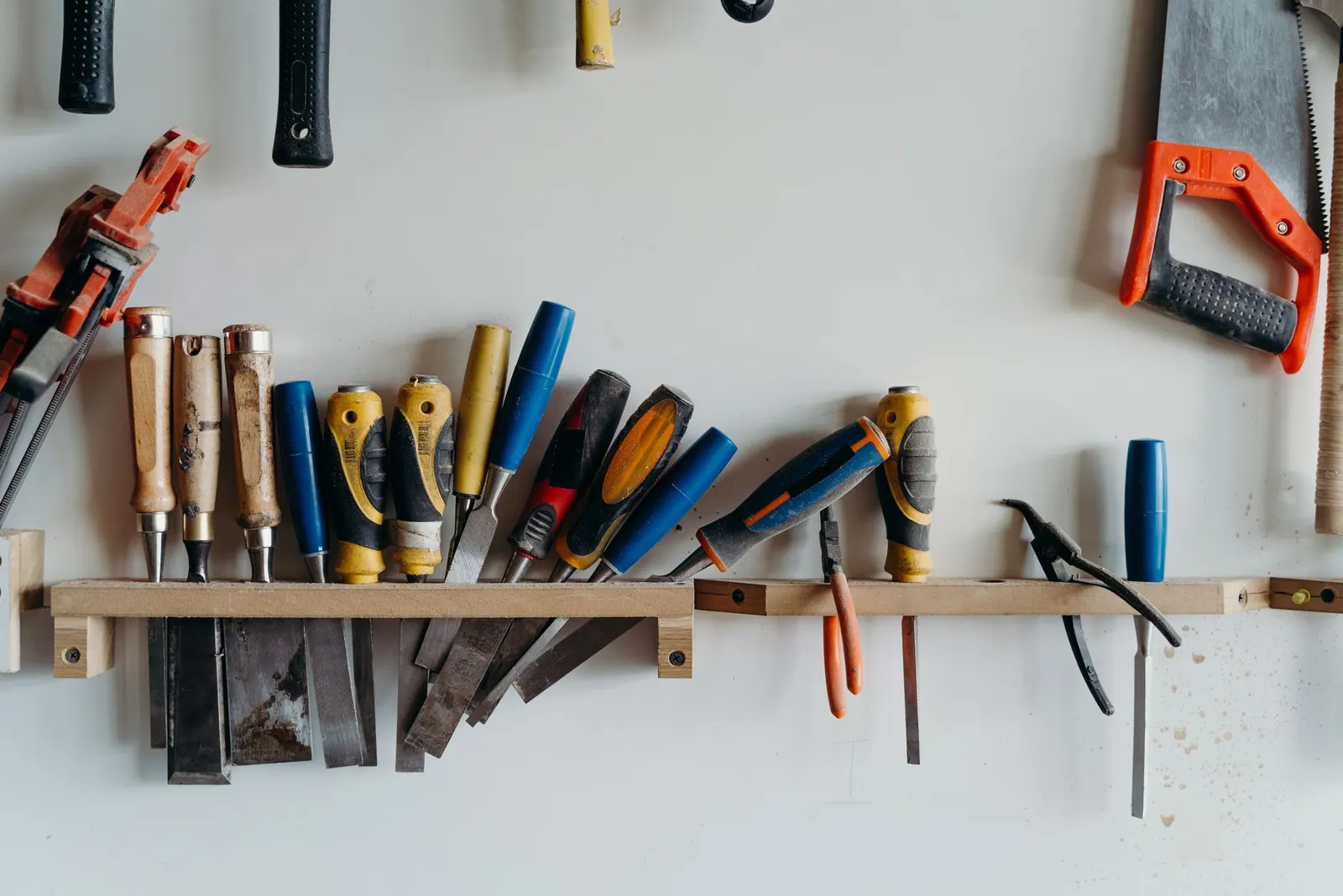 Ciseaux à bois, scie et tenailles rangés sur un support en bois fixé au mur de l’atelier.