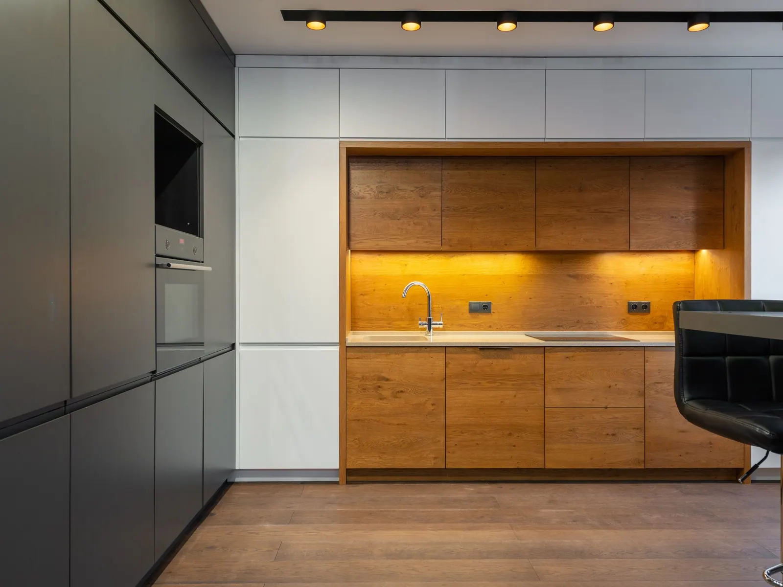 Cuisine sur mesure aux façades en chêne et blanches, niche éclairée et colonnes noires avec four encastré.