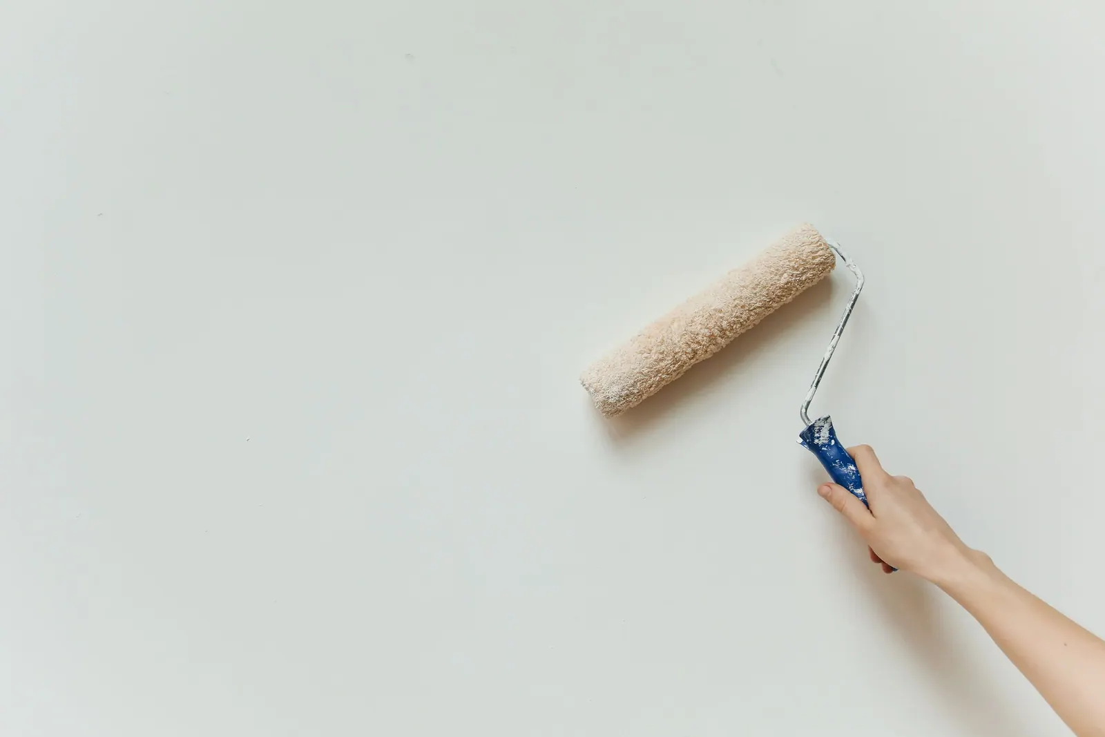 Main qui passe un rouleau de peinture sur un mur blanc.