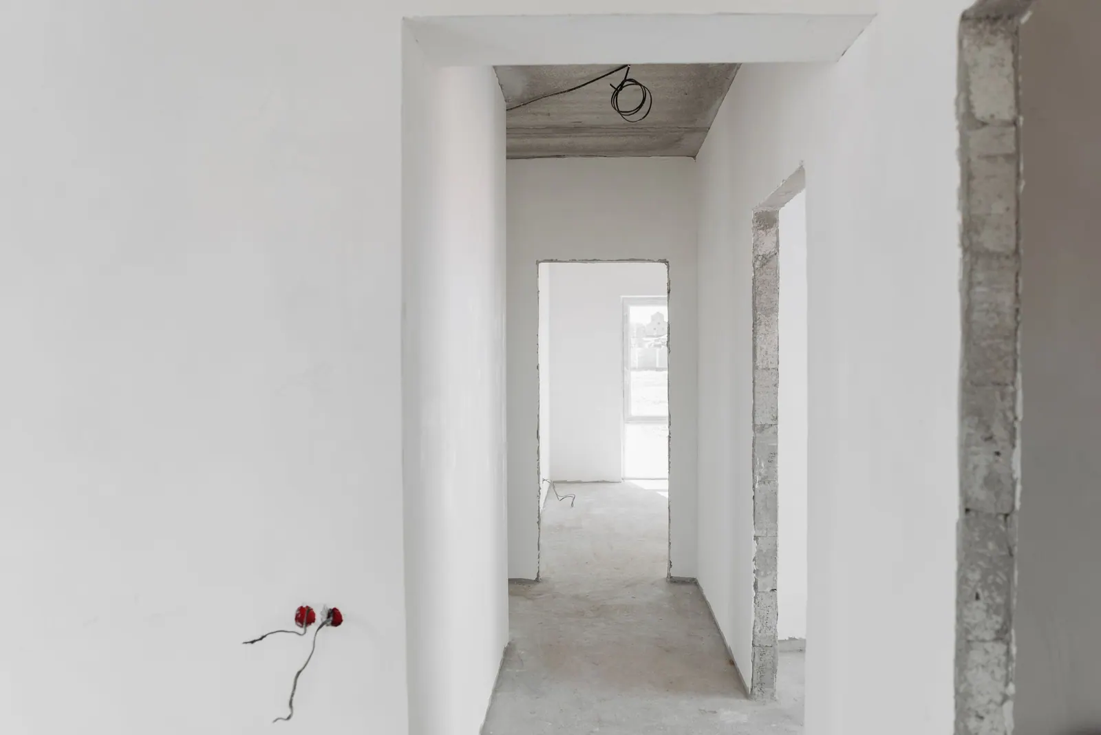 Couloir aux murs enduits et lissés en blanc, avec des prises en attente, prêt à recevoir la peinture.