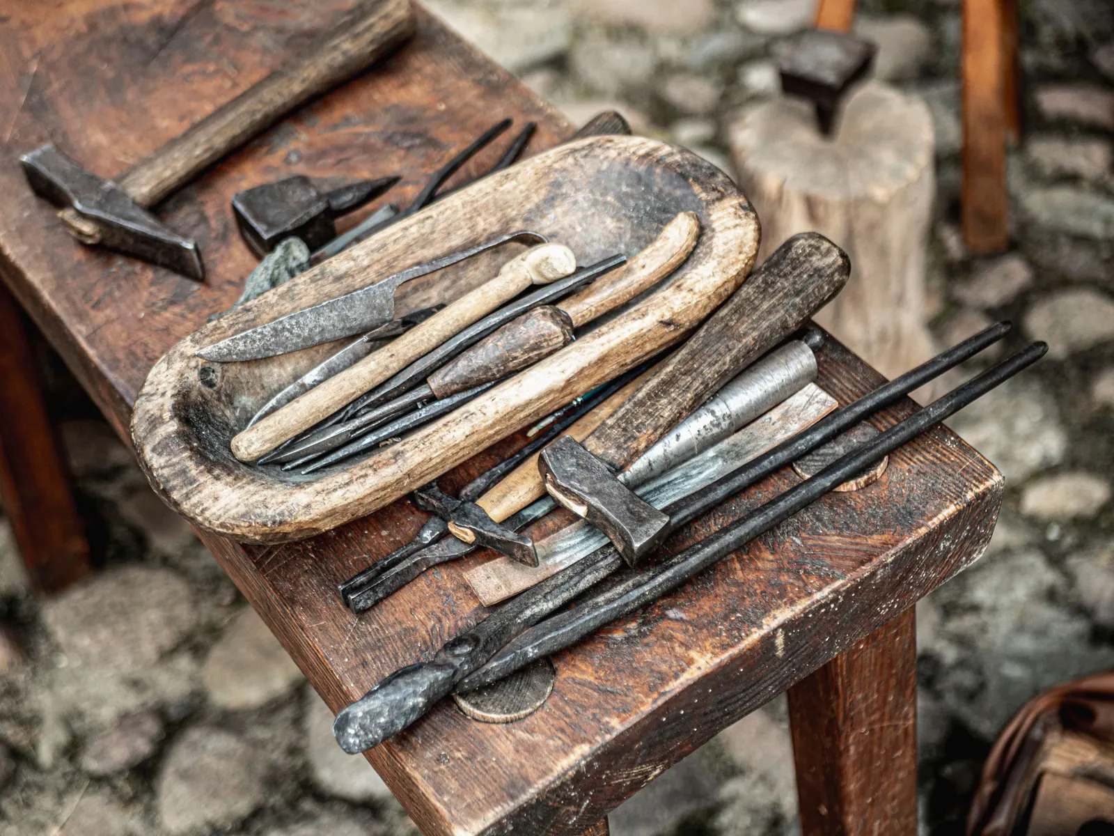 Outils de forge posés sur un banc en bois : marteaux, tenailles et burins.