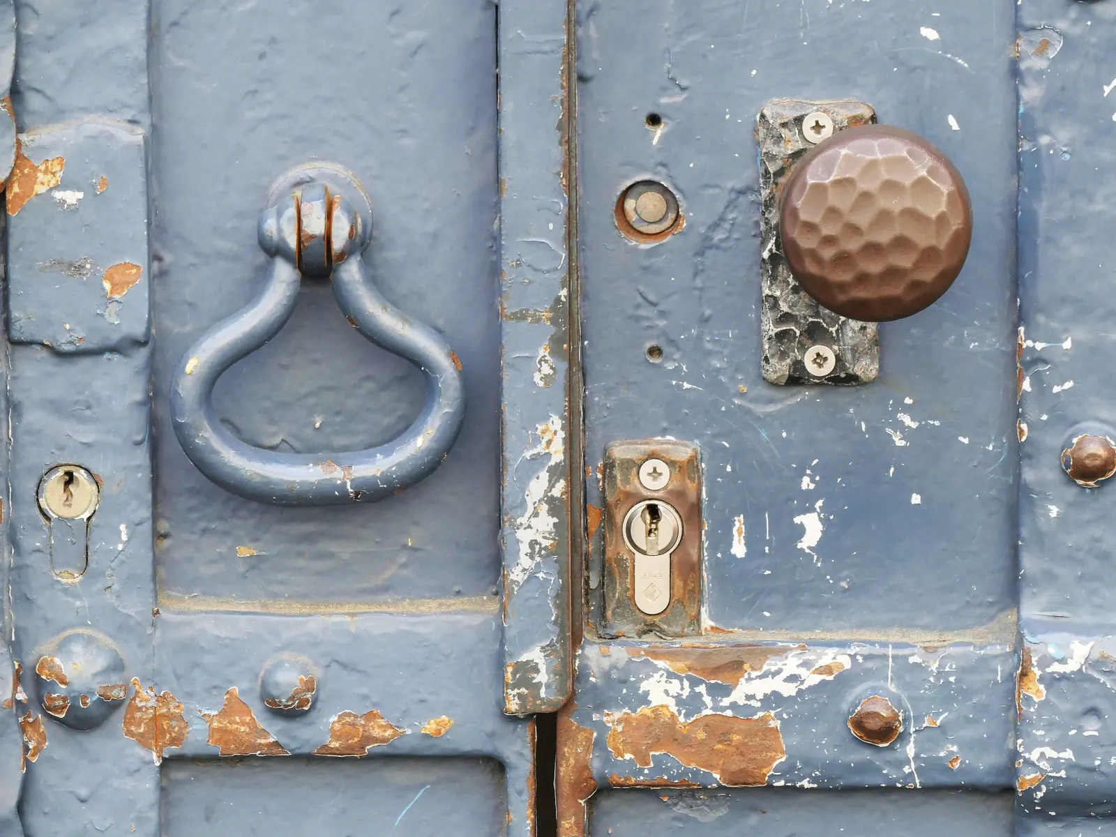 Vieille porte bleue à la peinture écaillée, avec heurtoir en fer, bouton de porte et serrure à cylindre usés.